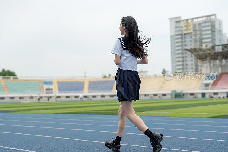 身穿白色制服的年轻亚洲女性在大学操场上锻炼、跑步和散步