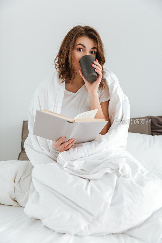 女士坐在床上，一边看书一边喝咖啡。