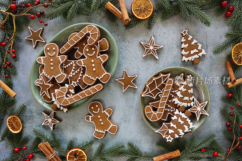 自制姜饼圣诞主题饼干的形象，在绿色的盘子里覆上白色的皇家糖霜，周围环绕着云杉针、红莓、肉桂棒、八角和柑橘干水果片