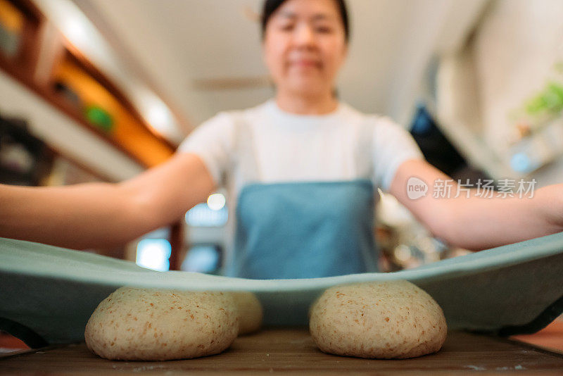 亚洲华人面包师妇女在厨房用布盖着面团