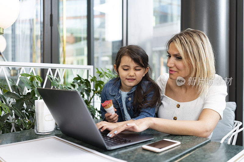 年轻的母亲和她的小女儿坐在咖啡馆，用笔记本电脑购物，做远程教育，玩游戏，看电影。