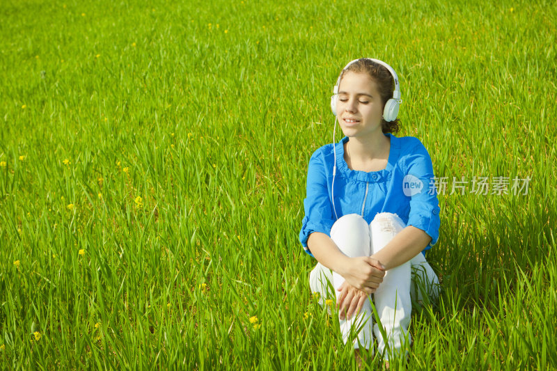 年轻女孩在绿色的田野里听着音乐