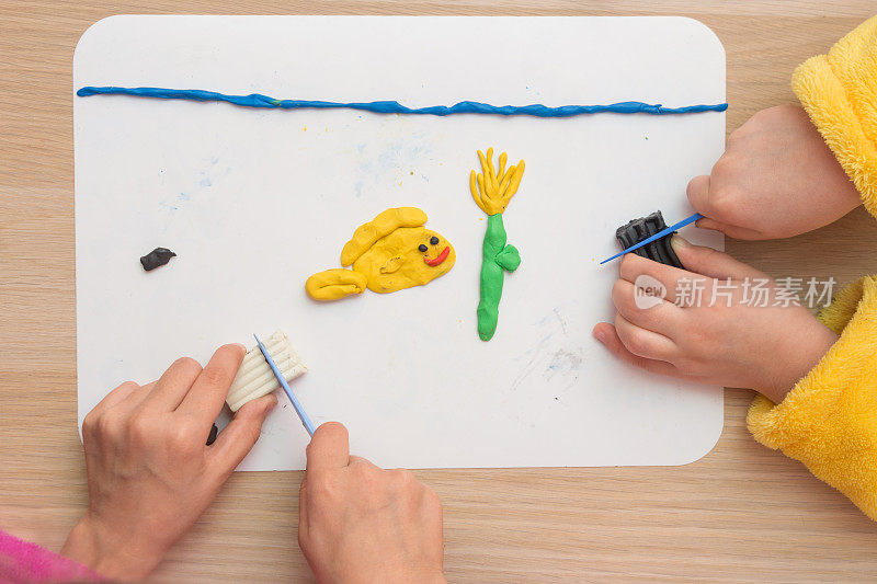 俯视图:两个孩子用粘土塑造在船上的鱼和海里的水下花朵