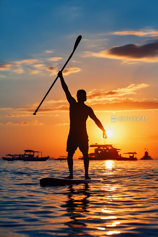 站在SUP上的划桨者的黑色日落剪影