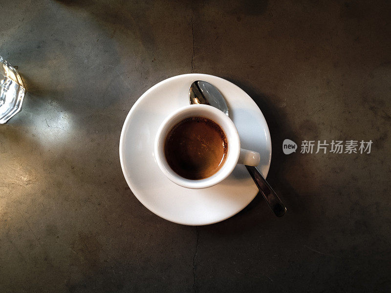 白色杯子里的浓咖啡放在深色的水泥桌上