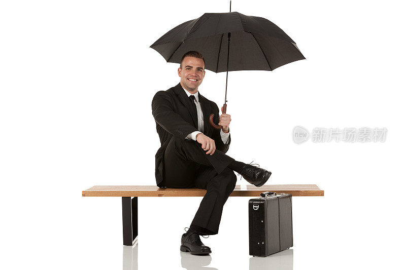 快乐的商人拿着伞坐在长椅上