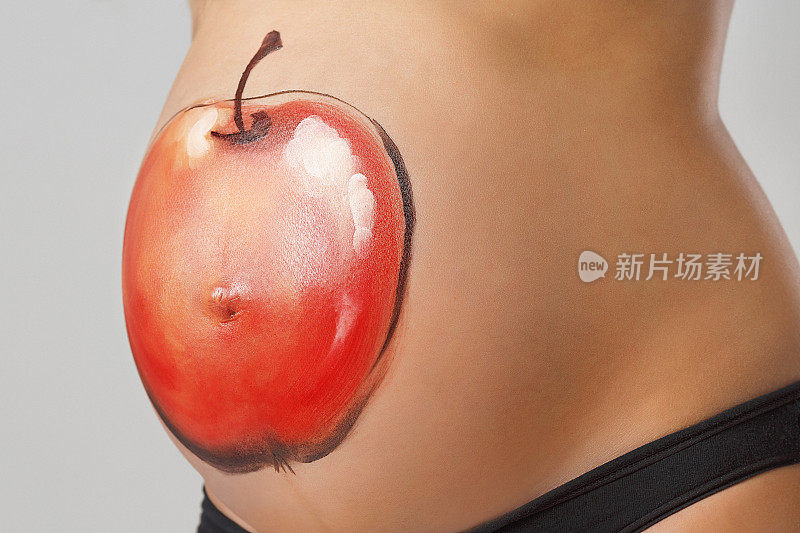 美丽的怀孕少女在孕妇的肚子上画苹果