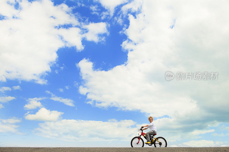 男孩骑着自行车，背靠夏天湛蓝的天空