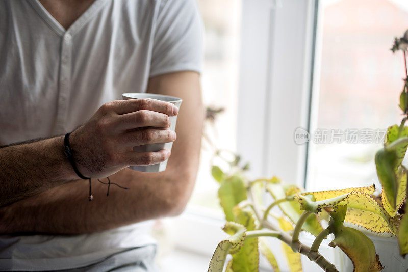 一个面目全非的男人拿着一杯咖啡坐在窗边。