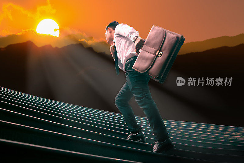 年轻的亚洲商人拿着一个棕色的皮包跑在楼梯上的剪影山和障碍与成功的阳光。