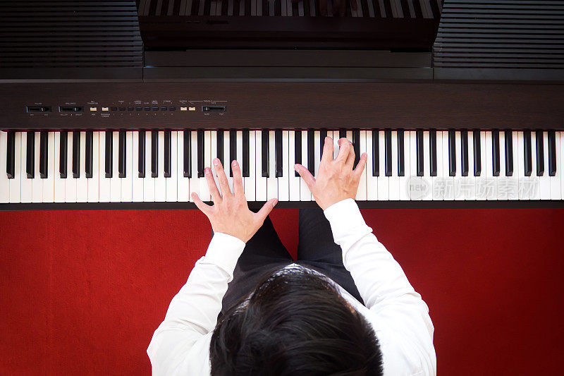 亚洲人弹钢琴。顶视图与红色地板背景。学习基本节奏和音乐技巧最喜欢的乐器。