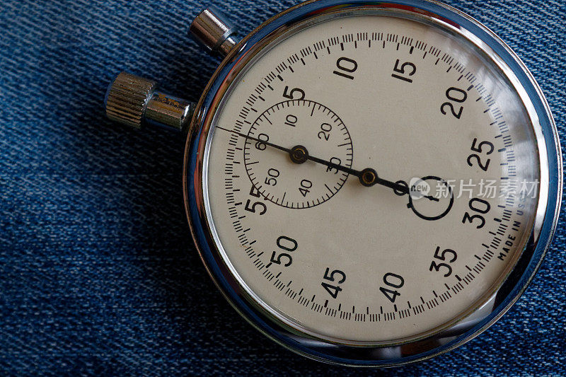 秒表在破旧的旧蓝色牛仔布背景下，值测量时间，旧时钟箭头分秒精确计时器记录