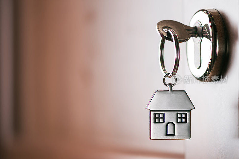 房子钥匙挂在一个房子形状的银钥匙圈上，锁在一扇棕色大门的锁上