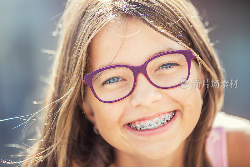 快乐的微笑女孩戴着牙套和眼镜。年轻可爱的白种金发女孩戴着牙套和眼镜
