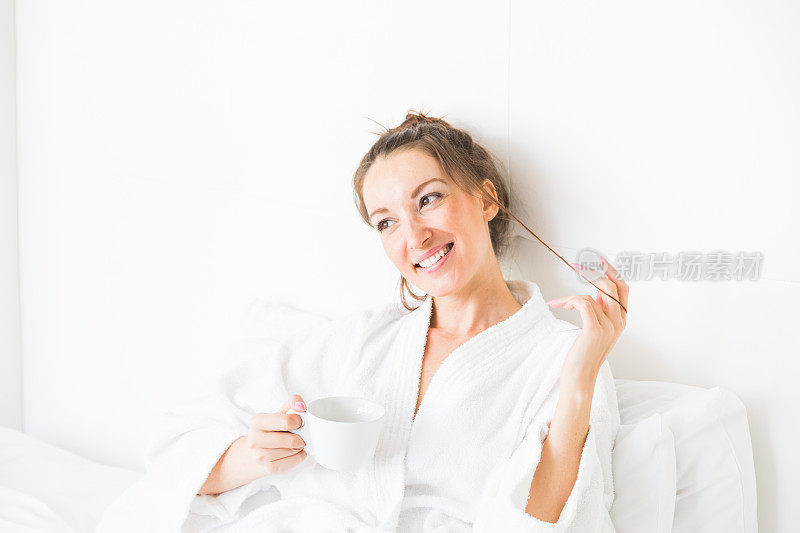 可爱的年轻女子在床上享受早晨的咖啡
