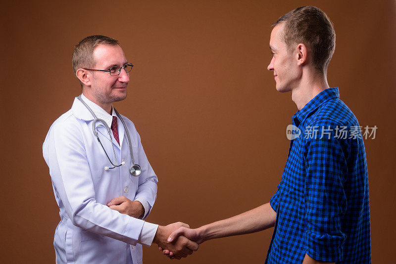 摄影室拍摄的男子医生与年轻男子病人在彩色背景下握手
