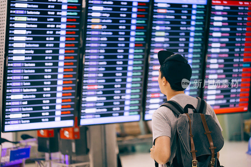 年轻男性旅客在登机时间监视器屏幕上观看和等待航班时间