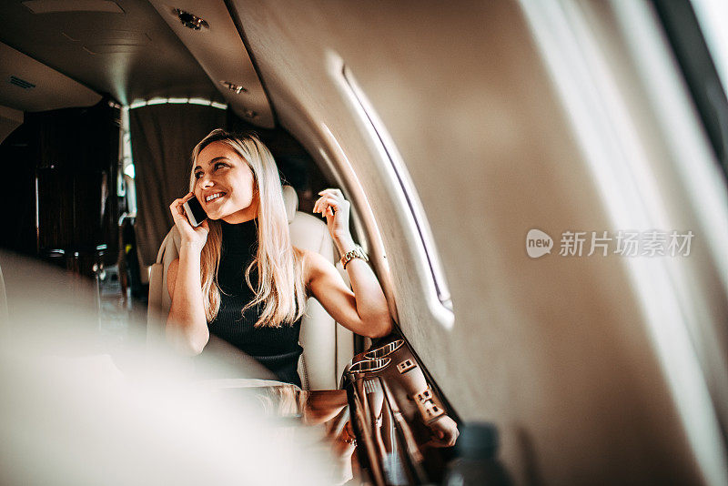 年轻的女商人在私人飞机上用智能手机聊天