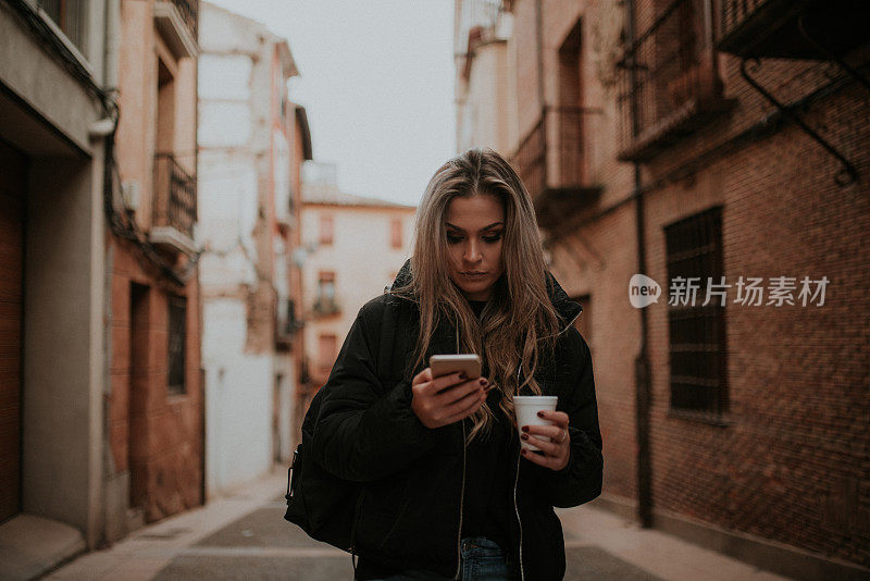 年轻女子拿着外带咖啡杯看着智能手机