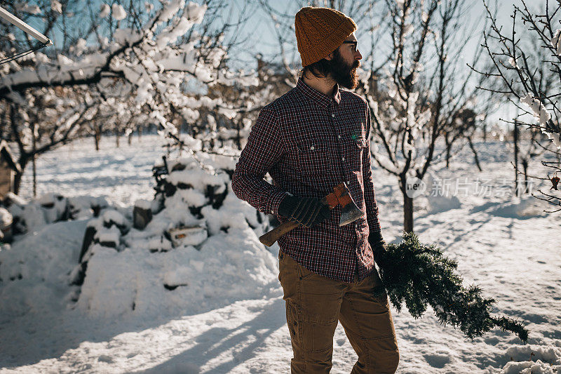 在大雪纷飞的冬日里，英俊的蓄着胡须的男人在户外挥舞着斧头