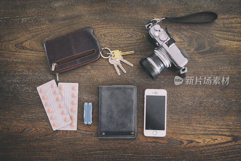 采购产品旅行配件包括，护照，药丸，相机，小刀，钥匙，和手机在一个木制的背景