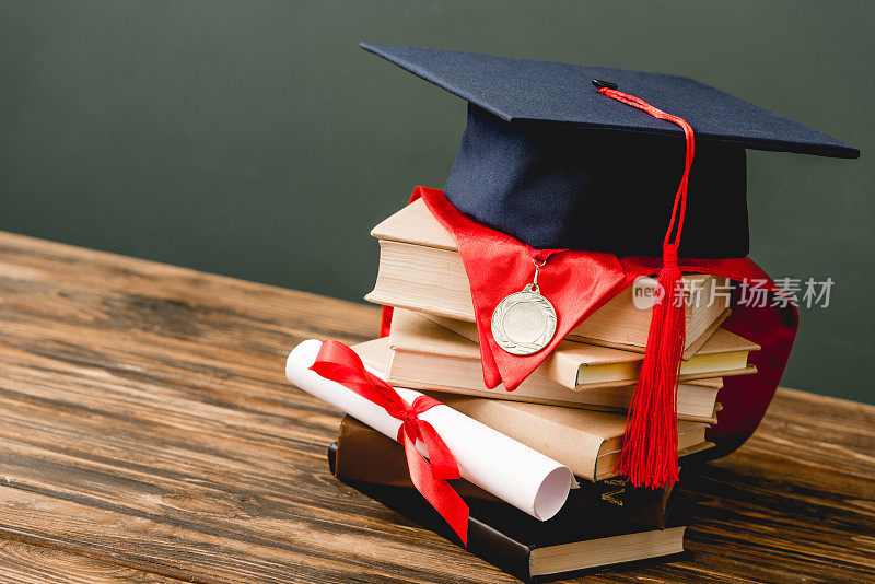 书籍，学术帽，奖章和文凭在木制表面孤立在灰色