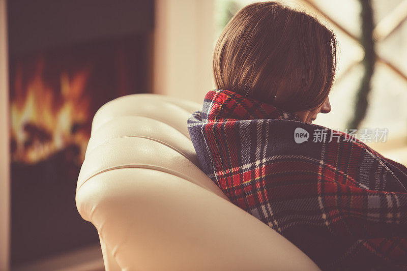 年轻女子裹着一条舒适的毯子，在壁炉旁放松