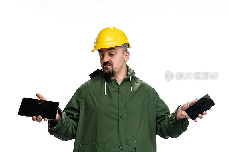 身穿绿色雨衣、头戴安全帽的年轻工程师手持平板电脑和智能手机，背景为白色