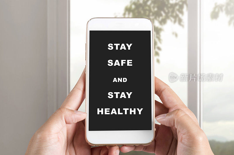 手拿着手机，屏幕上写着“保持安全，保持健康”的信息