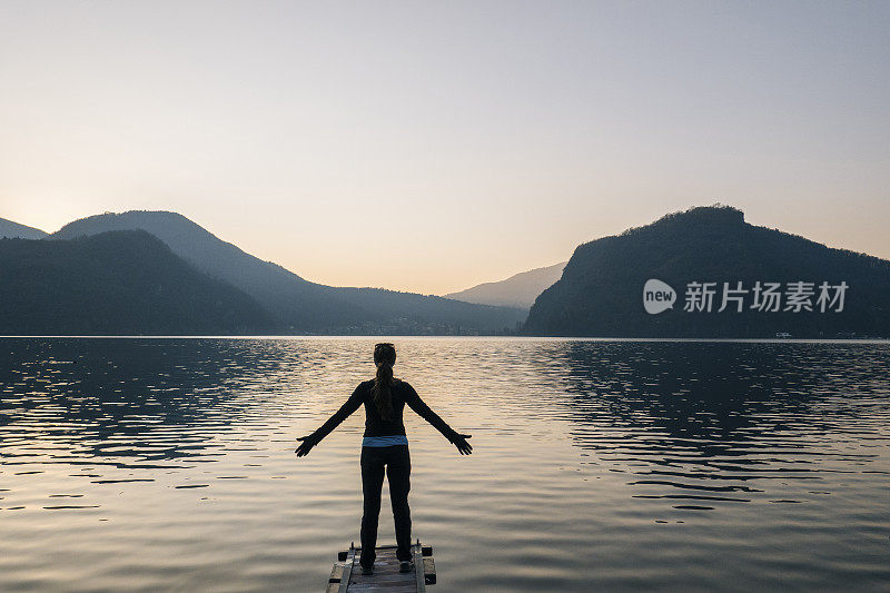 在码头的尽头，一名女子在湖上迎接日出