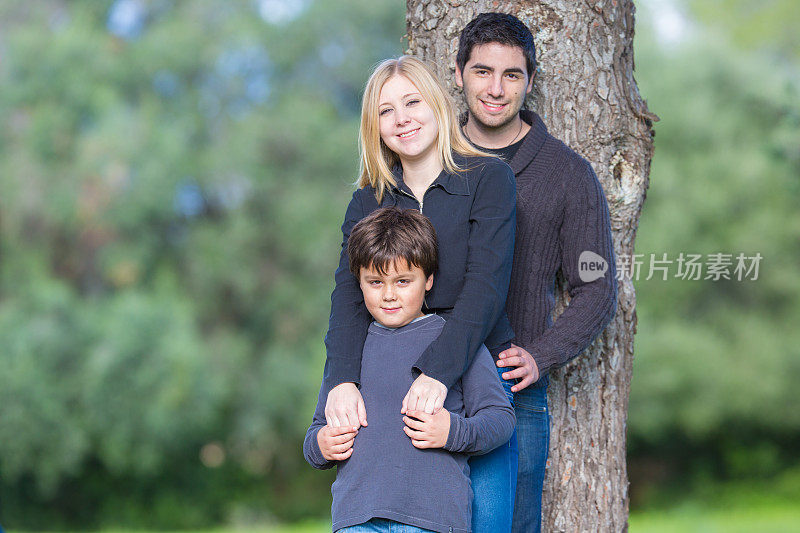 年轻夫妇和孩子拥抱，站在一棵树旁