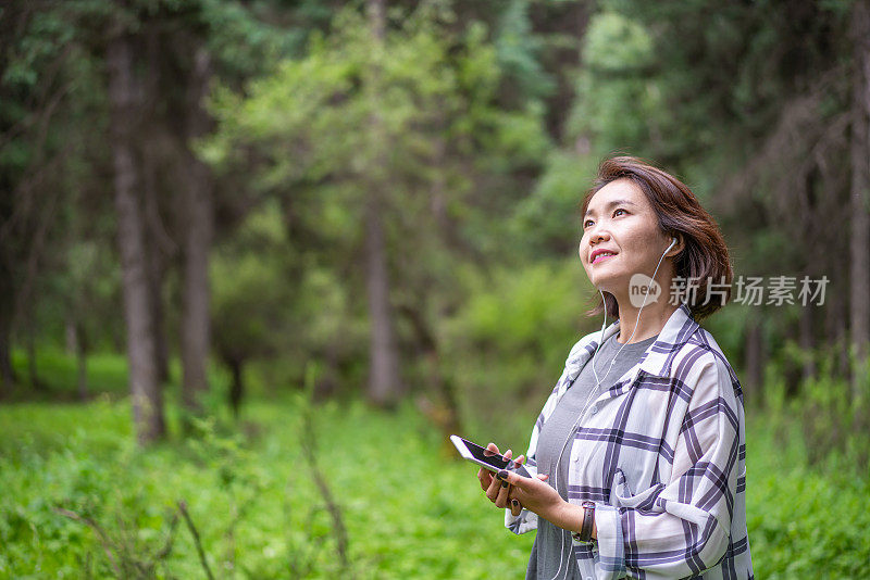 年轻的亚洲女子在森林里戴着耳机听音乐