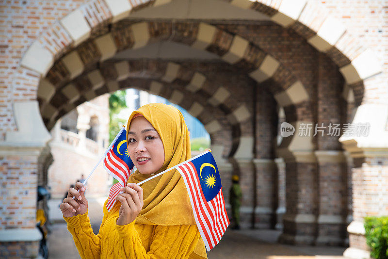 年轻的马来西亚妇女挥舞着马来西亚国旗，带着高昂的爱国主义精神庆祝独立日