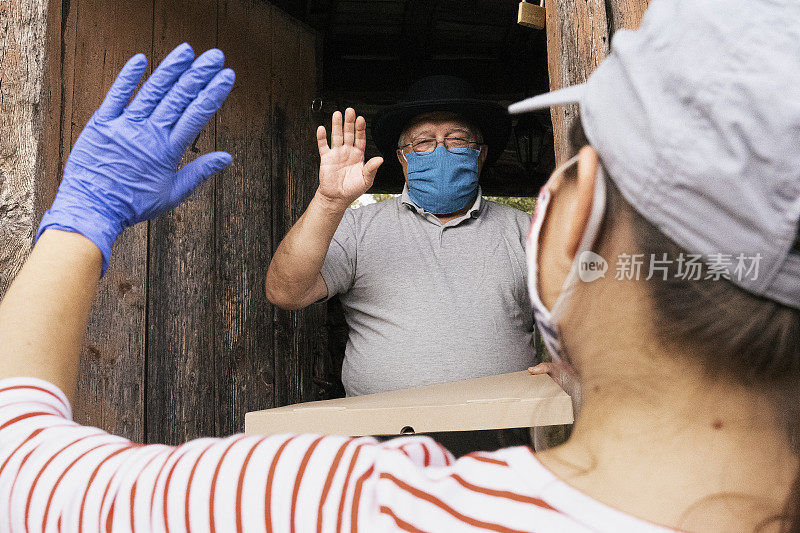 新的标准。居家送餐和冠状病毒防护。老人在家收披萨外卖，然后付钱。COVID-19大流行期间的疾病预防。戴着防护面具的人。