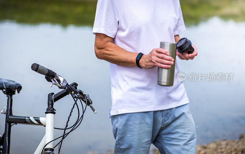 一名男子在湖边骑完自行车后拿着水瓶休息