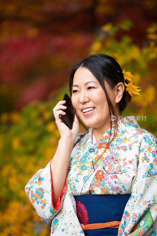 穿着和服的女人用秋天的枫叶打电话
