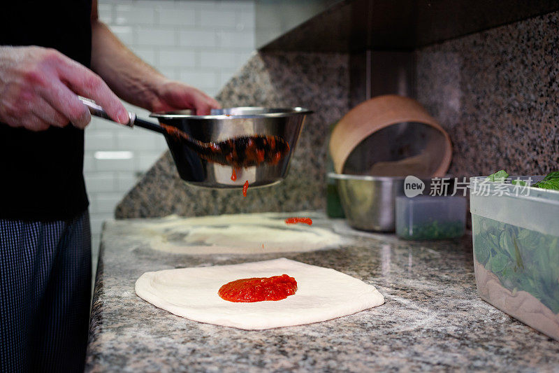 把番茄酱放在餐厅厨房柜台上的披萨面团上