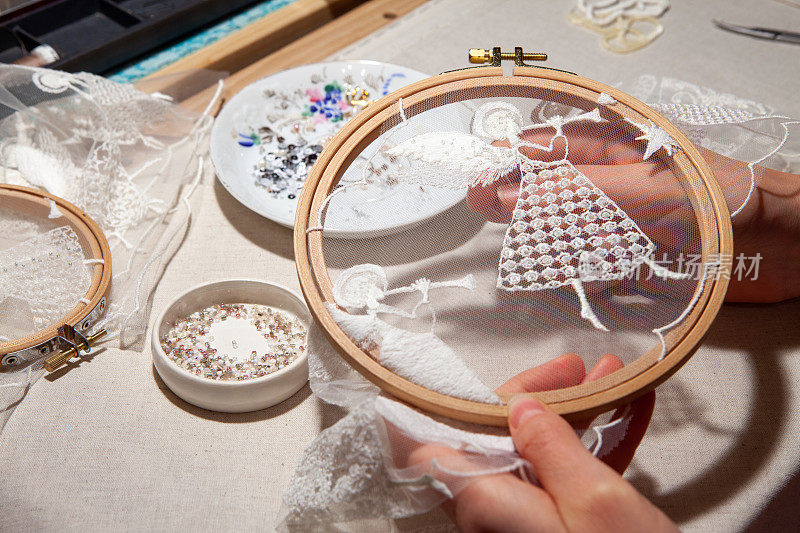 一个绣工的工作场所与刺绣框架，天使刺绣，珠子。绣工的手拿着绣箍