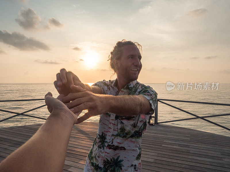 一对夫妇在日落时在木制码头上牵手，热带度假