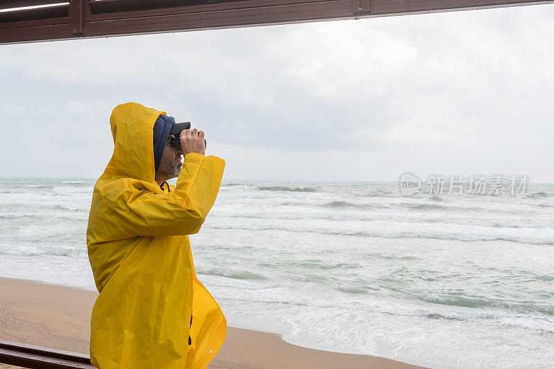 穿雨衣的人在屋顶阳台上用双筒望远镜看海。