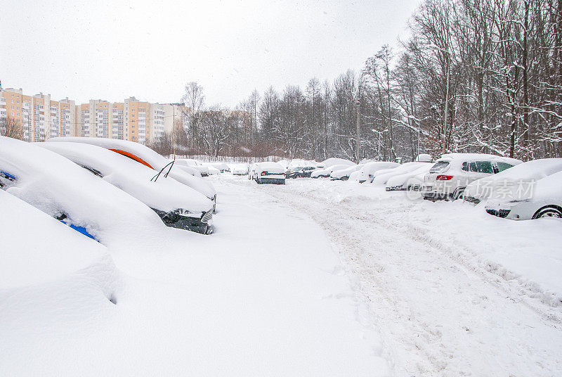 白雪覆盖的街道，道路和汽车在雪下。暴风雪，暴风雪交通。天气气候灾难。冬天的城市风光。雪后的雪堆