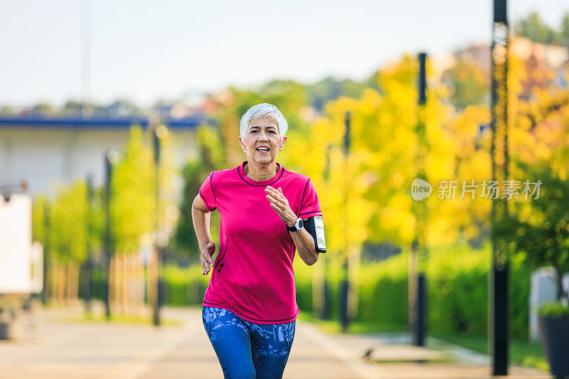 女老年人在城市公园的道路上跑步。成熟的跑步女性在户外训练，享受自然。夏天早上做有氧运动。老年人健康的生活方式