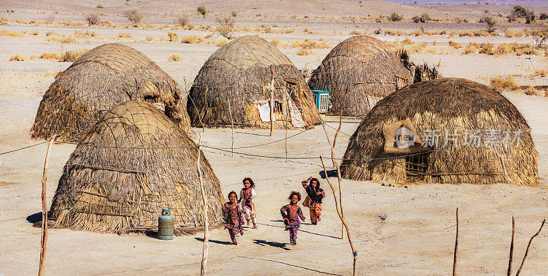 伊朗锡斯坦和俾路支省的尼克沙赫尔县，俾路支省的孩子们在他们的传统房屋旁玩耍。