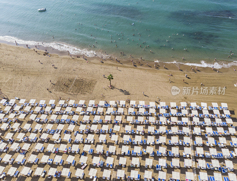在土耳其安塔利亚，一个炎热的夏天，沙滩上有很多太阳躺椅和太阳床的鸟瞰图