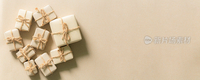 棕色的礼物，棕色的圣诞节礼物，礼品盒包装在牛皮纸与白色，银色和金色的丝带和蝴蝶结在柔和的米色背景。空白礼物标签的文本。节日礼物的概念。前视图。