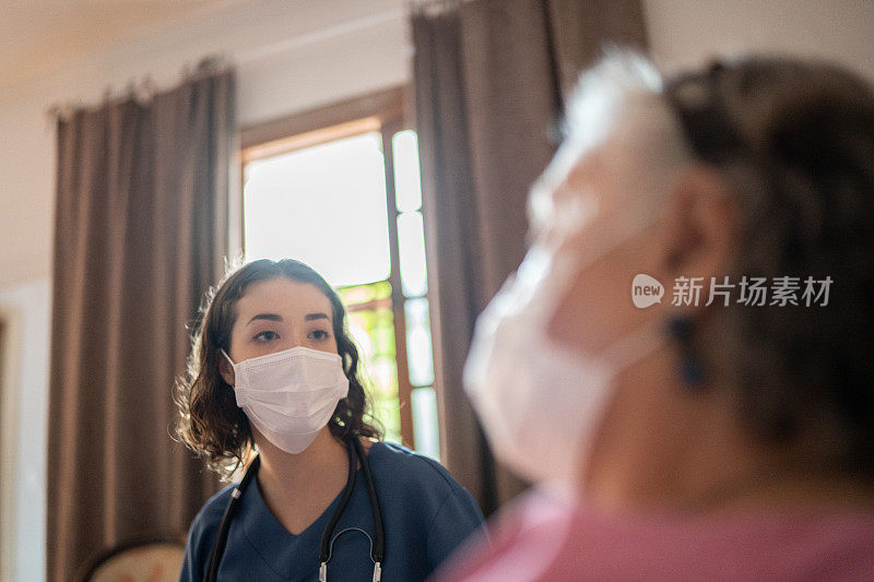 护士戴着口罩与家中的老年病人交谈