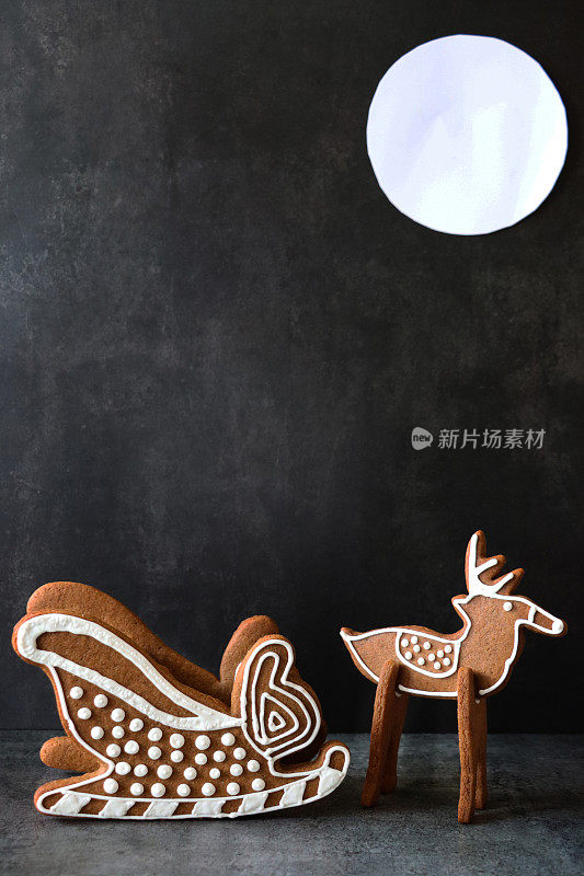 近景自制，姜饼饼干驯鹿和雪橇，用白色皇家糖霜装饰，夜晚黑色背景与满月