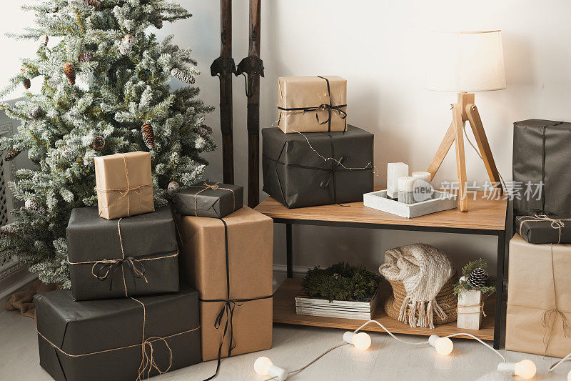 时尚的室内在斯堪的纳维亚风格的冬季假期与自然圣诞树，花环和许多礼物在牛皮纸