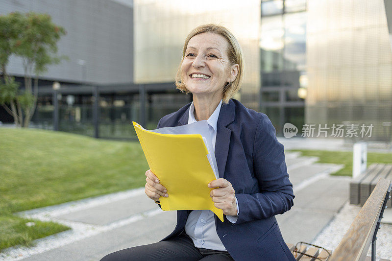 商务女性在长椅上休息时笑着拿着文件夹