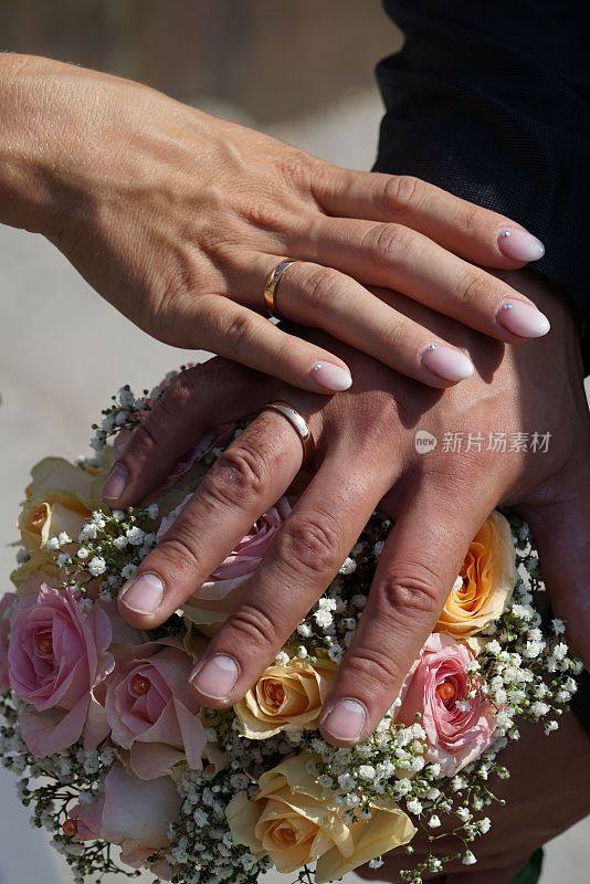 垂直特写的新娘和新郎展示他们的结婚戒指在一束花